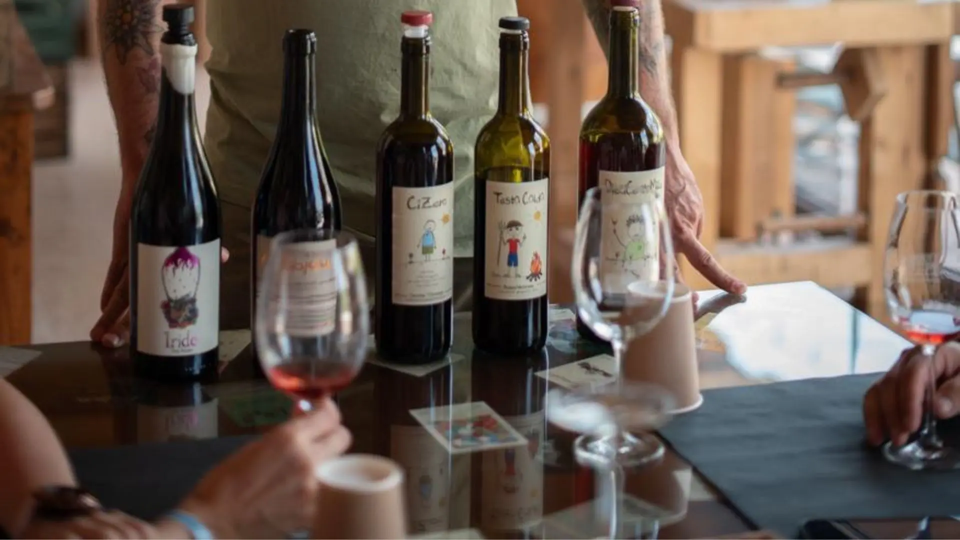 Terre di Pietra wine tasting. There are five wine bottles on a table, as well as three different wine glasses. A person is explaining something to the people present.