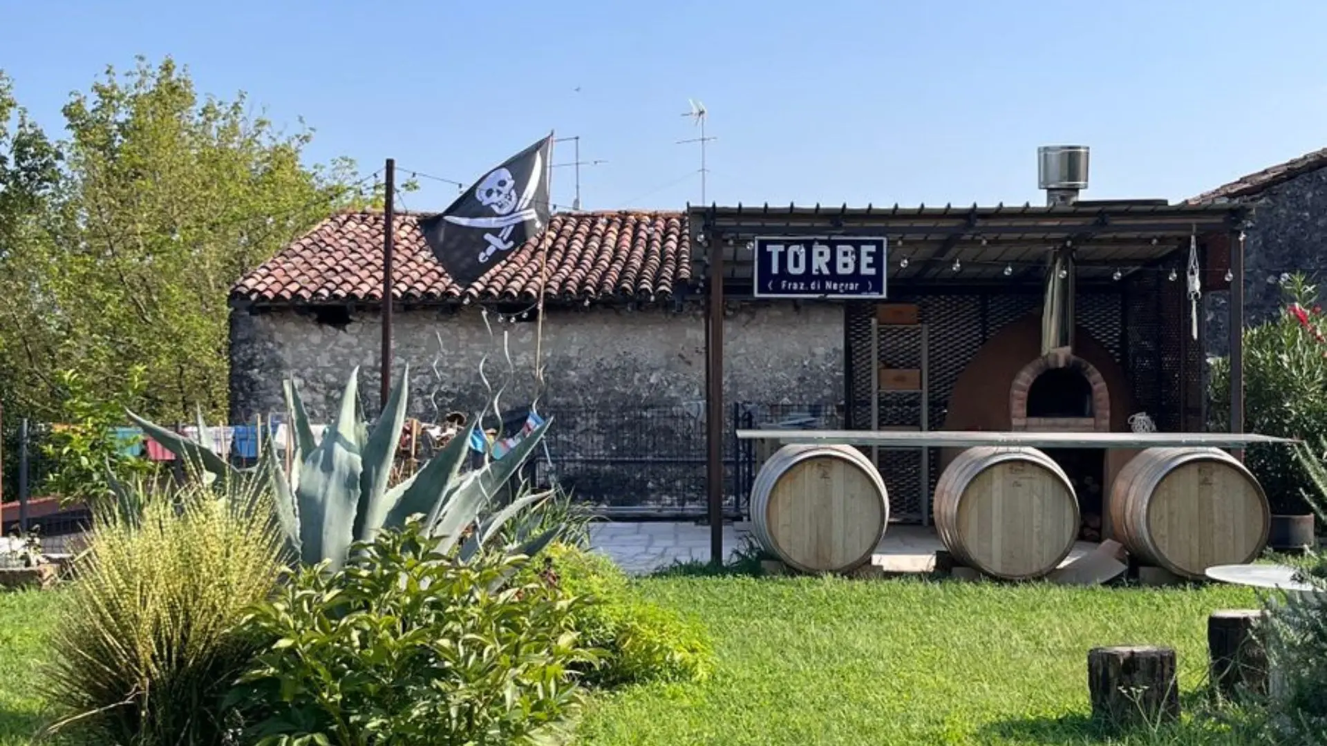 The courtyard of the Terre di Pietra winery in the Veneto region in Italy. There is a pirate flag on a pole, and various wine barrels, three of them used to support a makeshift bar.