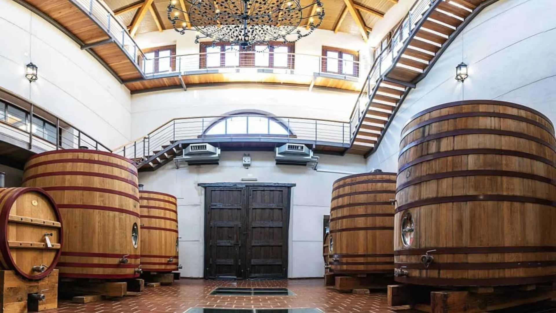 Bodega Mont Reaga wine tanks and barrels can be seen near each wall of the room. We are facing a huge double door and there is a staircase leading to two distinct floors above. The entire space is open and the tanks can be seen from each of the floors.