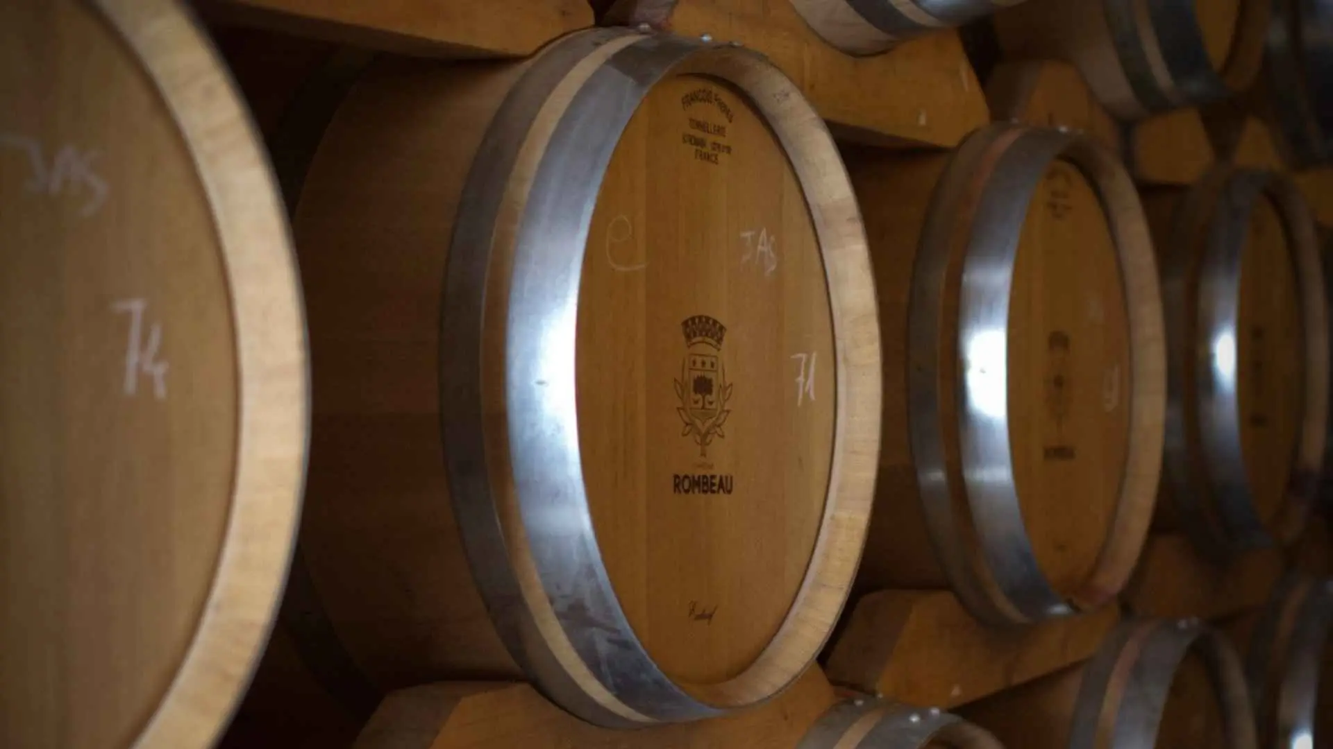 Domaine de Rombeau wine barrels in the cellar. They are stacked on top of one another.