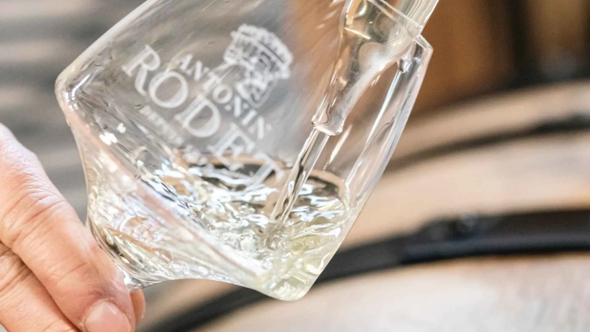 A closeup of a wine glass while someone is pouring wine. There is an Antonin Rodet inscription on the glass.