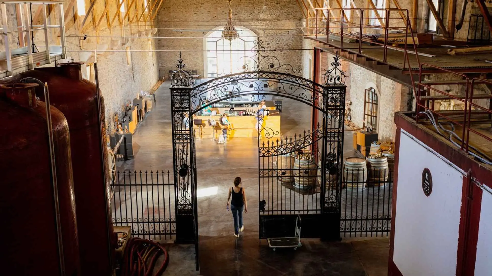Château de Paraza winery interior, with huge wine tanks. People can be seen in the middle, seated at a bar.
