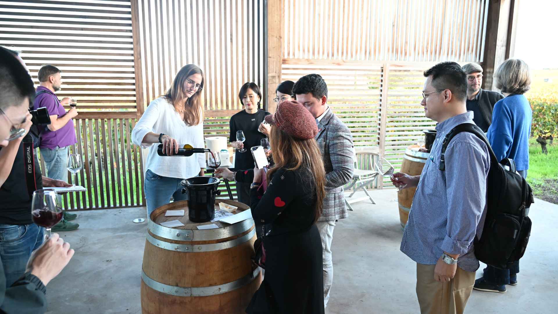 The photo shows various tourists having a wine tasting experience. The barrels are used as tables and people are drinking wine and chatting.