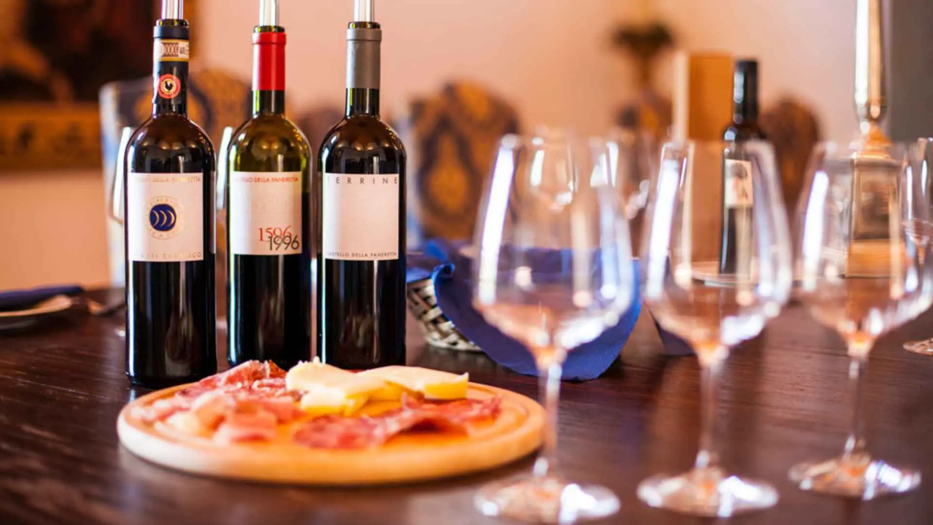 A set table with three wine bottles, three glasses and food on a wooden plate. This is a wine tasting experience at the Castello della Paneretta winery.