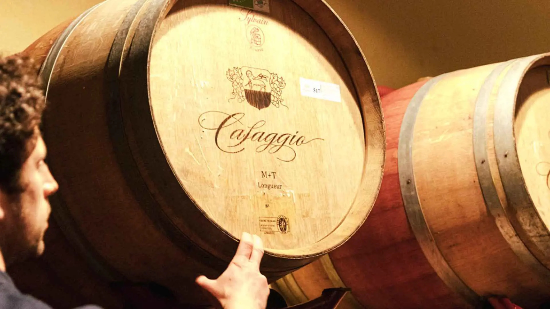 Caffagio winery wine barrels with a cursive inscription of the brand name on the lid, as well as a worker pointing toward the barrel.