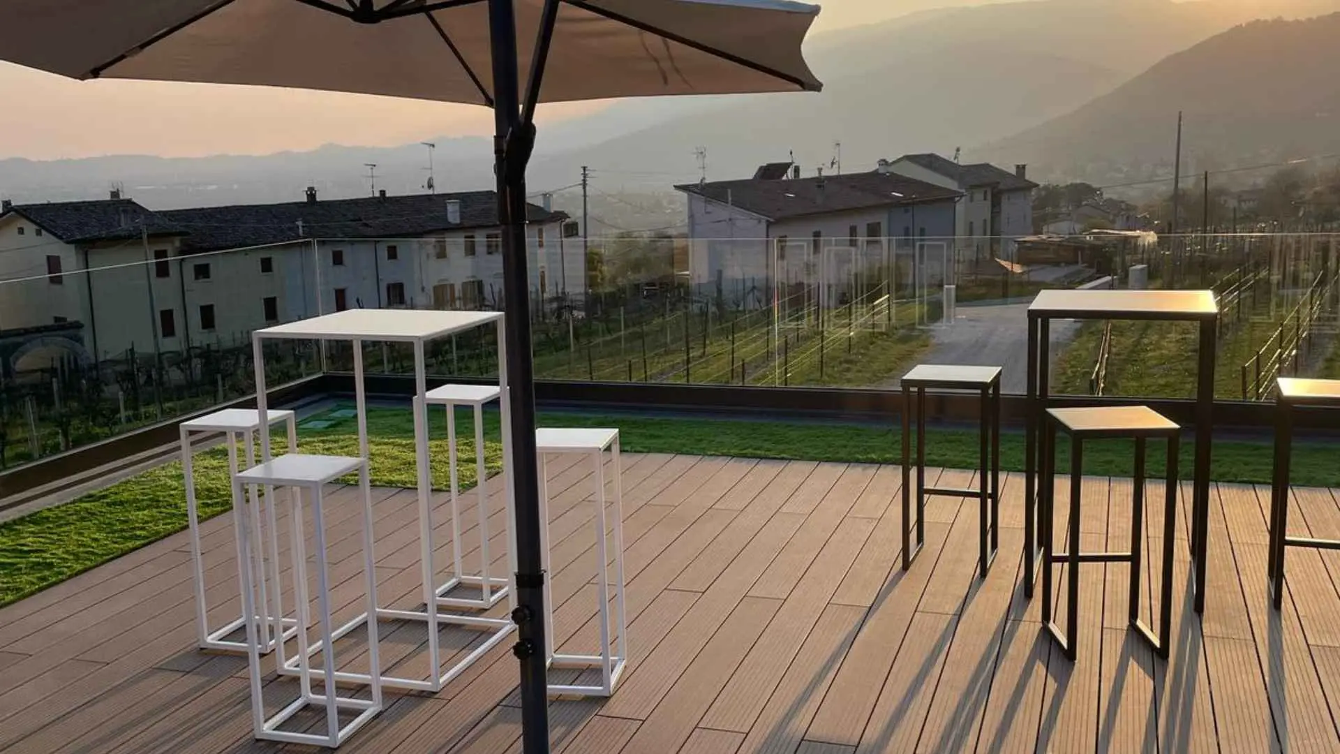 High tables and chairs and an umbrella at the Azienda Agricola Rivaluce winery during a sunset.