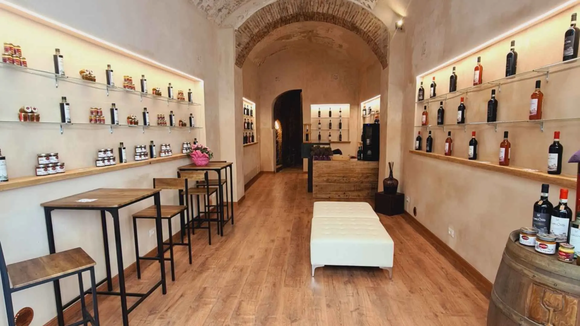 The interior of the Borgunto Wine & Oil winery. The image shows tables on the left, as well as high chairs. There are two divans in the middle. Each of the walls has various wine bottles and products, ready for tasting.