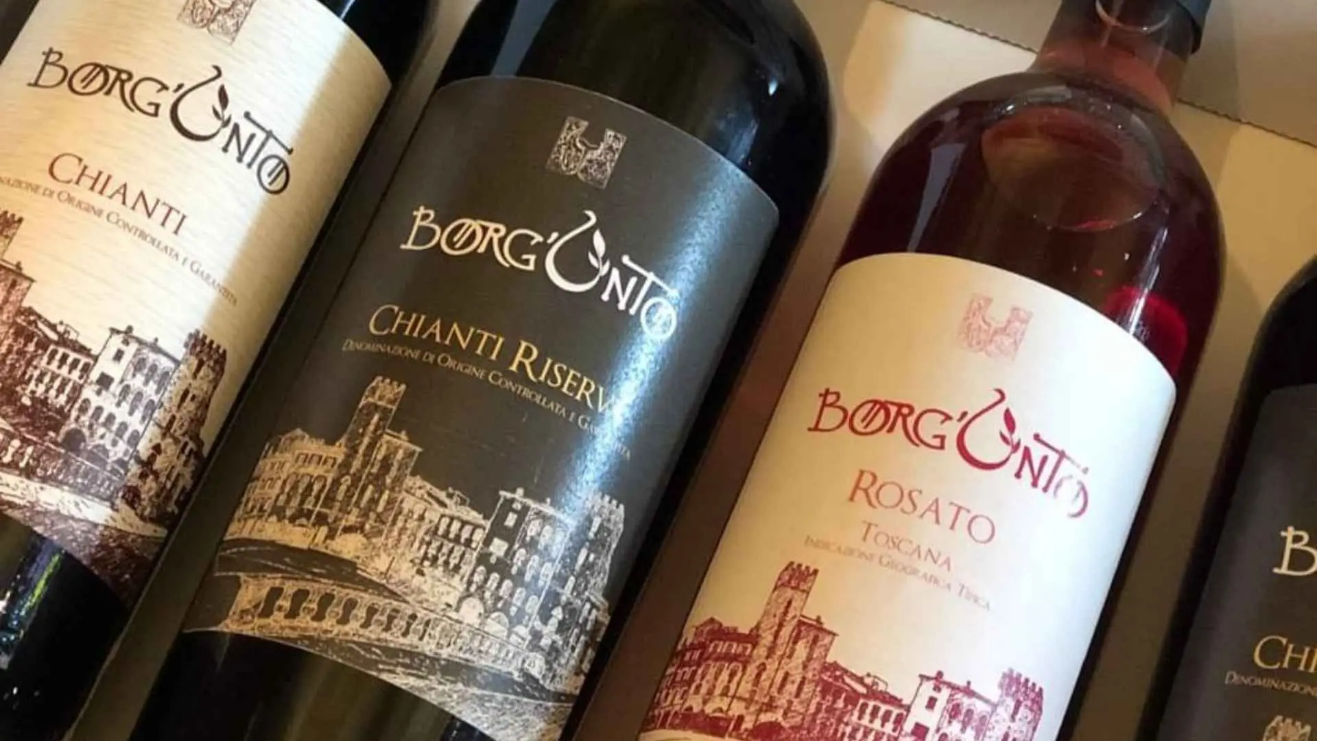 A closeup of three Borgunto Wine & Oil wine bottles. They hold distinct wines and the stickers reflect that.