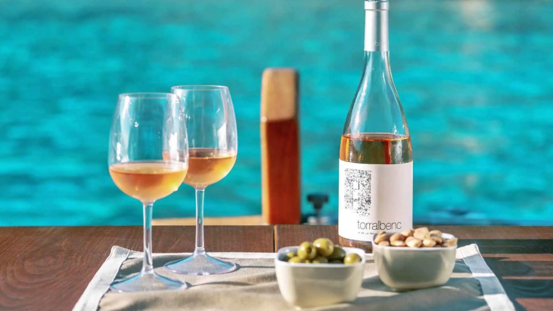 Bodega Torralbenc wine tasting experience. You can see two wine glasses, olives and peanuts, as well a wine bottle, overlooking the sea.