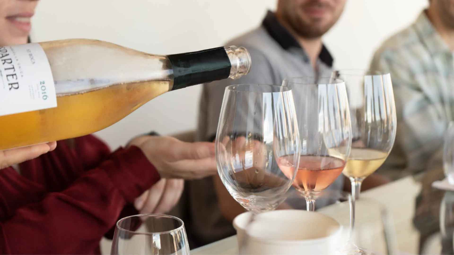 Three people and three glasses can be seen. A bottle is also in focus, preparing to pour wine in one of the glasses, at the AT Roca winery in Spain.