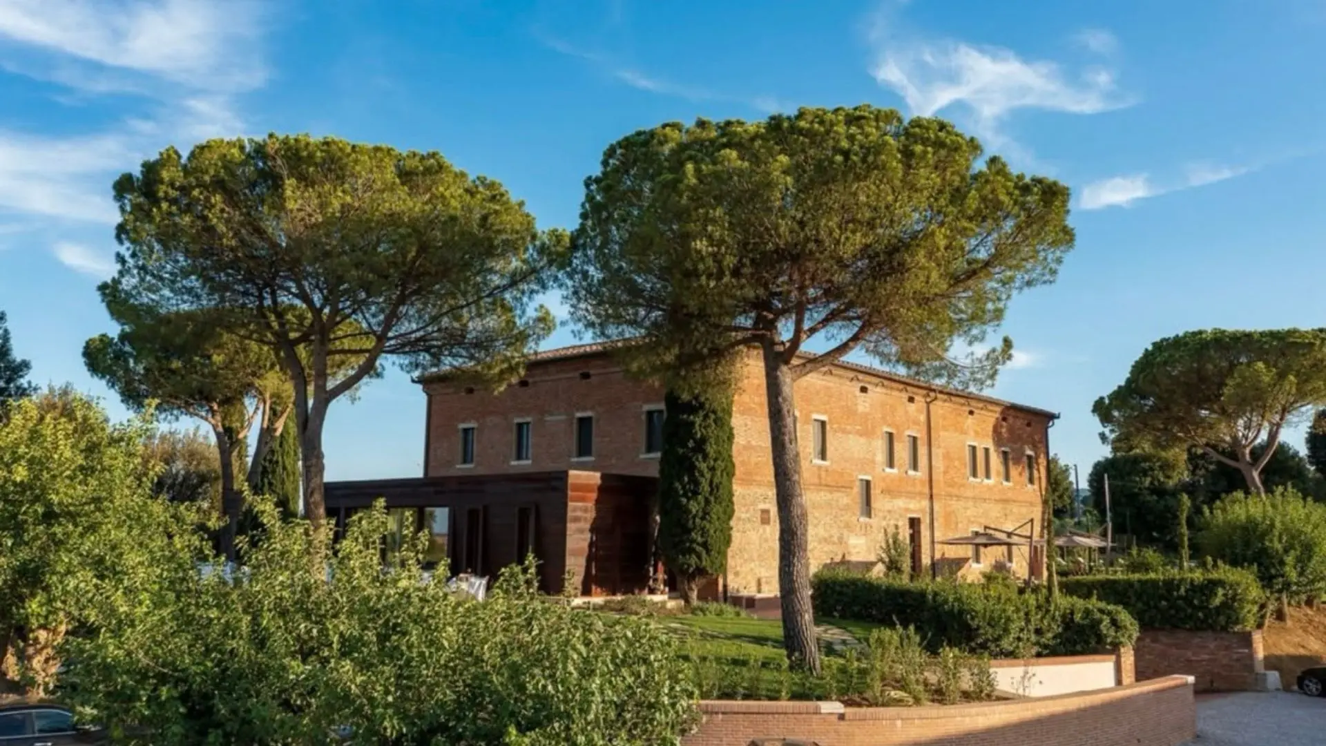 Fattoria Svetoni, a winery in an old building. We can see the building, but parts of it are behind a tree and bushes. The upper part of the image shows a blue sky. 