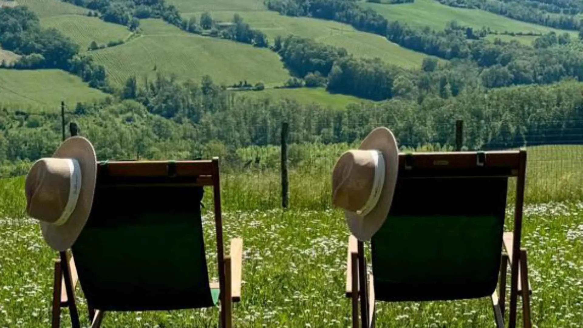 The image shows two chairs with two hats on them. The chairs are overlooking green fields.