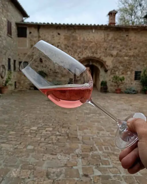 A glass of rose wine, in focus. The glass is tilted. There is a stone courtyard in the background.