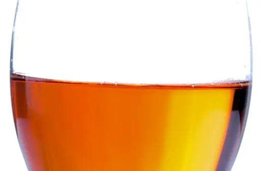 A glass of orange wine against a white background. The wine is see-through and has a distinct orange tint.
