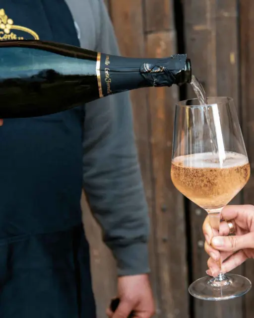A bottle and glass of sparkling wine. The wine is being poured into the glass.