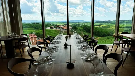 A set table at the Scurek winery in Slovenia. The table is looking out at the vast vineyard and natural surroundings, through a modern, floor to ceiling wall of windows.