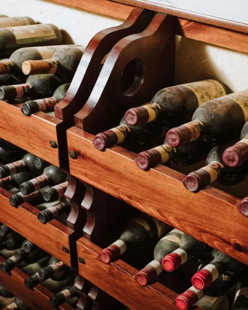 Wine bottles, stored on a shelf, horizontally, two rows of bottles per shelf.